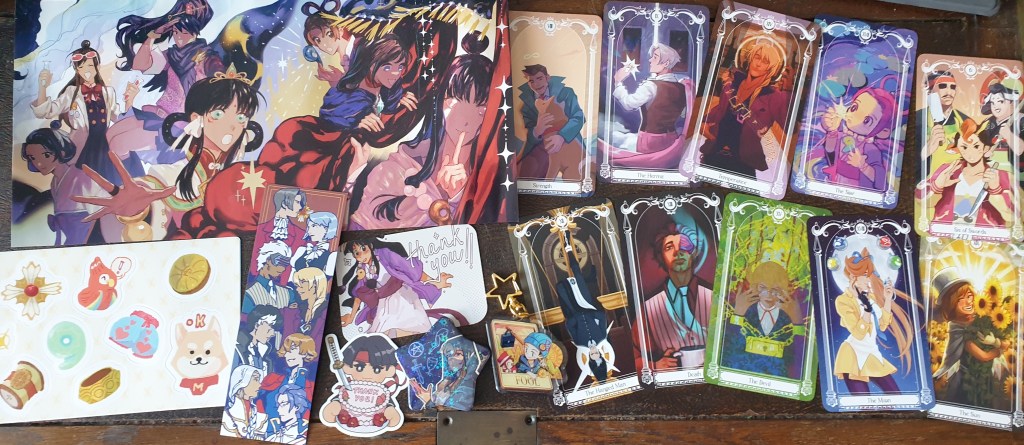 a photograph of my turnabout tarot haul: a print, stickers, a bookmark, a thank you card and sticker, a two-sided acrylic charm, a button, and a selection of cards, largely major arcana.